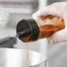 A hand in a glove pouring red spice from a container with a 48/485 Black Dual Flapper Heat Induction-Lined Lid into a bowl.