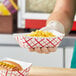 A hand holding a Southern Champion red checkered paper food tray with macaroni and cheese and a hot dog with mustard.