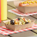 A hot dog with mustard and a bowl of pasta salad in a Southern Champion kraft paper food tray on a table.