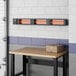A Boltic black electric infrared heater with a black frame above a wooden table.