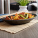 A black Elite Global Solutions Zen oval plate with food and chopsticks on a table.