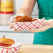 A woman holding a red and white checkered paper food tray of fried chicken nuggets in front of a hamburger.