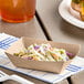 A Southern Champion kraft paper food tray with coleslaw and a hamburger on a table.