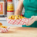 A woman in a green apron holding a Southern Champion red checkered paper food tray of french fries.