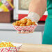 A hand holding a Southern Champion red checkered paper food tray filled with fried food.