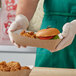 A person in a white apron holding a Southern Champion paper food tray of food.