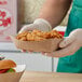 A person in gloves holding a Southern Champion paper food tray of chicken and fries.