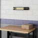 A Boltic black electric infrared heater mounted on a wall above a table in a bar.