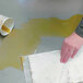 A hand holding a Quick Dam absorbent mat over a dirty floor.