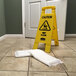 A yellow caution sign next to a white Quick Dam absorbent mat on a wet floor.