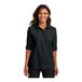 A woman wearing a black Port Authority short sleeve button down shirt.