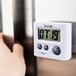 A close up of a hand holding a white Taylor digital kitchen timer.