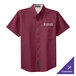 A close-up of a burgundy and light stone short sleeve dress shirt with a logo.