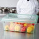 A chef standing in a school kitchen in front of a Carlisle green food storage box filled with yellow peppers.