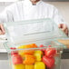 A chef in a white coat holding a Carlisle food storage container filled with red and yellow bell peppers.