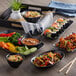 A black rectangular melamine tray with bowls of rice, noodles, and shrimp and vegetables on a table.