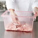 A person in gloves putting raw meat into a Carlisle red plastic food storage box.