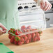 A gloved hand using a plastic clamshell container to cut strawberries.