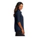 A woman standing and smiling wearing a navy Port Authority short sleeve shirt.