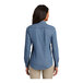 A woman wearing a faded blue Port & Company short sleeve denim button-down shirt.