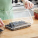 A gloved hand using a clear plastic clamshell container to put blueberries in.