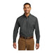 A man wearing a graphite Port Authority long sleeve poplin shirt and brown pants.