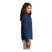 A woman wearing a medium ink blue Port & Company short sleeve denim button-down shirt.