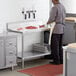 A man in a kitchen with a Regency stainless steel undershelf on a work table cutting meat.