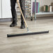 A man using a metal pole with a green handle to clean a floor with a squeegee.