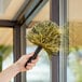 A hand holding a black Ettore Elite 8000 Cobweb Duster to clean a window.