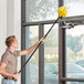 A man using an Ettore cobweb duster with extension pole to clean a window.