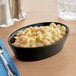 An Acopa black stoneware bowl filled with macaroni and cheese on a table.