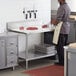 A man in a kitchen cutting meat on a Regency adjustable work table with a stainless steel undershelf.