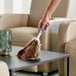 A hand holding an Ettore ostrich feather duster over a glass table.