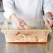 A person in a white coat holding a Carlisle yellow food storage box with raw chicken inside.