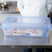 A person in a white coat holding a Carlisle blue plastic lid over a large container of food.