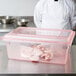 A chef in a white coat and pink gloves using a red Carlisle food storage box to hold raw meat.