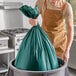 A man in an apron putting a Trinity Plastics green trash bag in a white trash can.