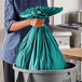 A person in a blue shirt holding a green Trinity Plastics garbage bag over a trash can.