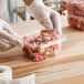 A person in gloves holding a Choice clear plastic container of candy.