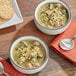 Two bowls of Kettle Cuisine Italian Wedding Soup with meatballs and vegetables on a table with crackers and a spoon.