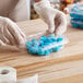 A person in a glove using a Choice clear plastic rectangular container to hold blue candies.