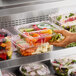 A hand holding a Choice clear plastic container of fresh vegetables.