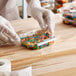 A person in gloves holding a Choice clear plastic container full of colorful candies.