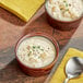 Two bowls of Kettle Cuisine New England Clam Chowder with a spoon on a yellow cloth.