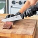 A person in black gloves using a Victorinox Churrasco Slicing Knife to cut meat on a cutting board.