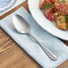 An Acopa Josette stainless steel serving spoon on a napkin next to a plate of food.