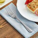 An Acopa stainless steel table fork on a napkin next to a plate of food.