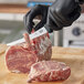 A person in black gloves using a Victorinox curved boning knife to cut meat on a wooden cutting board.