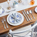 A table set with white and blue plates, a fork, and an Acopa Josette steak knife.